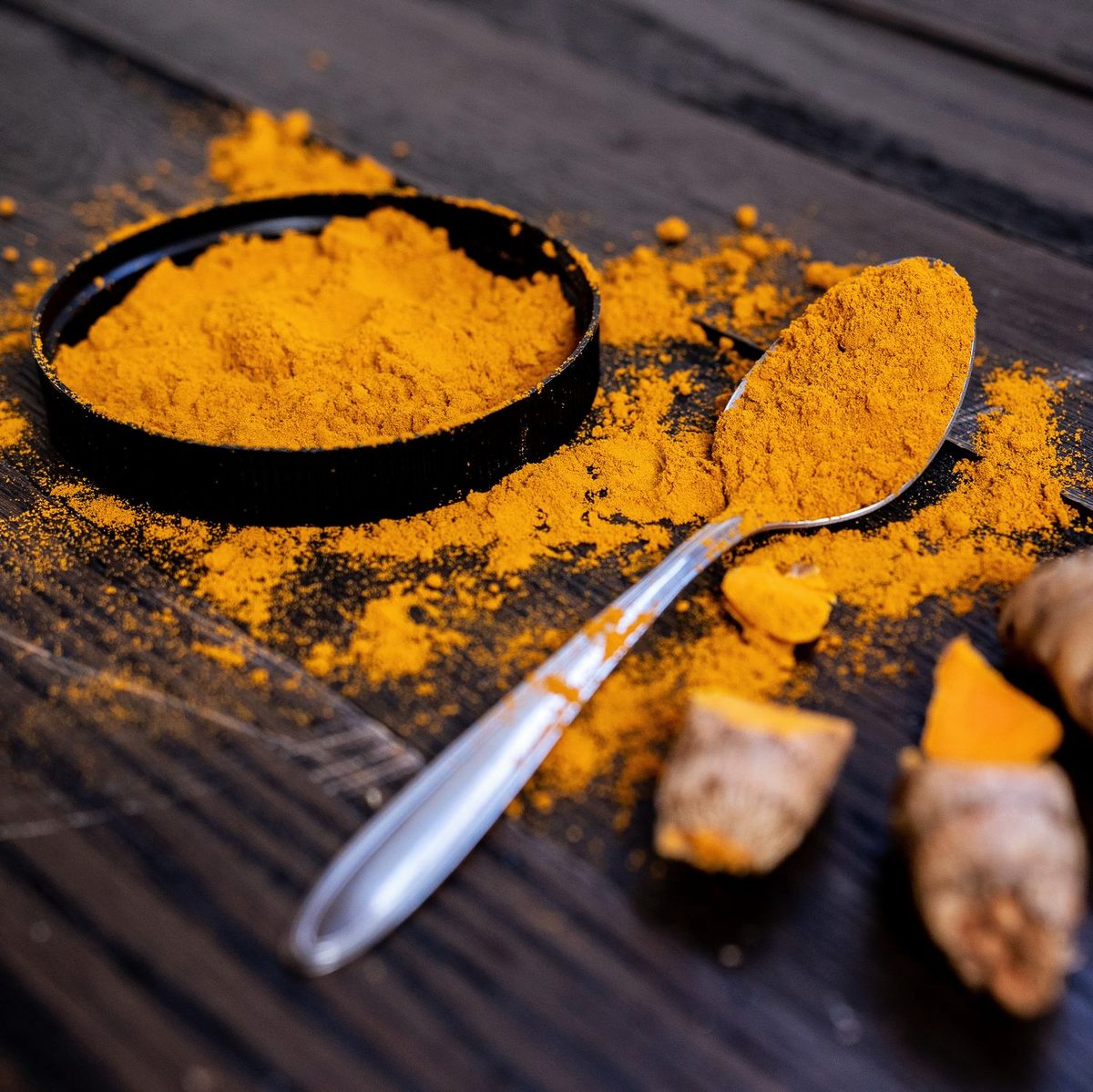 Turmeric powder in a black dish with a spoon and dried rhizomes on dark wood