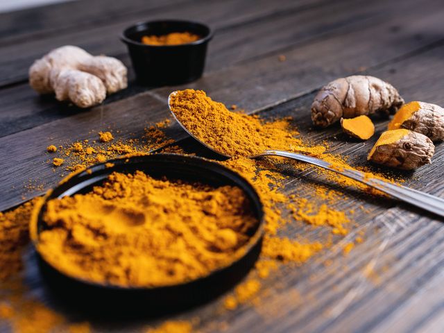 Ground turmeric beside dried turmeric and ginger root